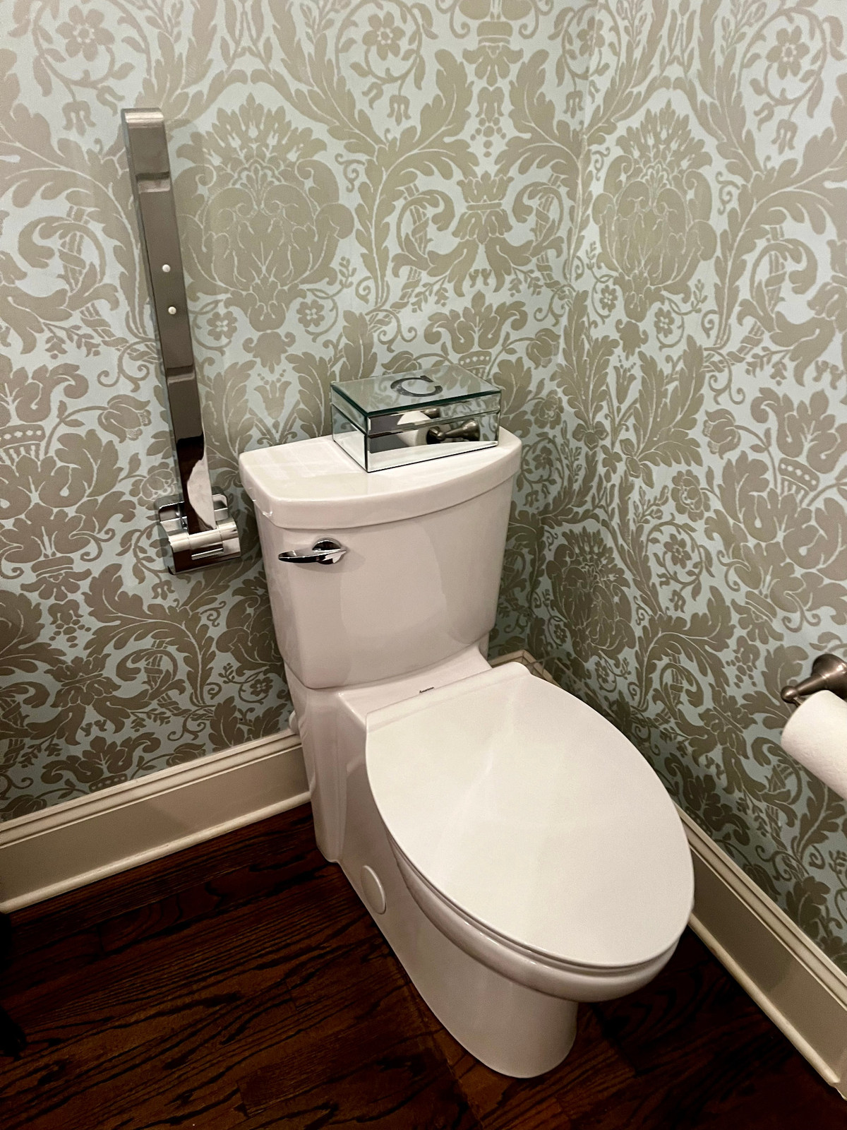 Support rail folded upright beside a toilet in a wallpapered powder room