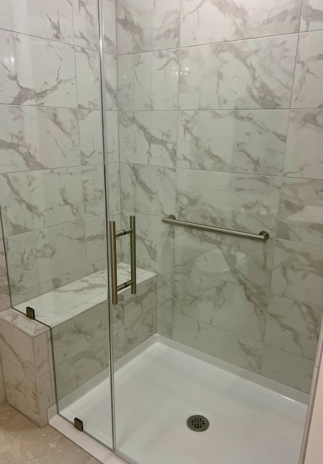 A walk-in shower with a built-in tiled bench, a horizontal grab bar and a low-profile shower base